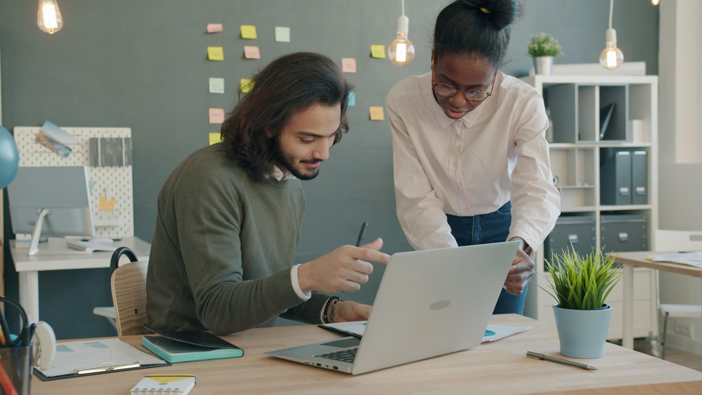 Two professionals review content on a laptop at a desk.